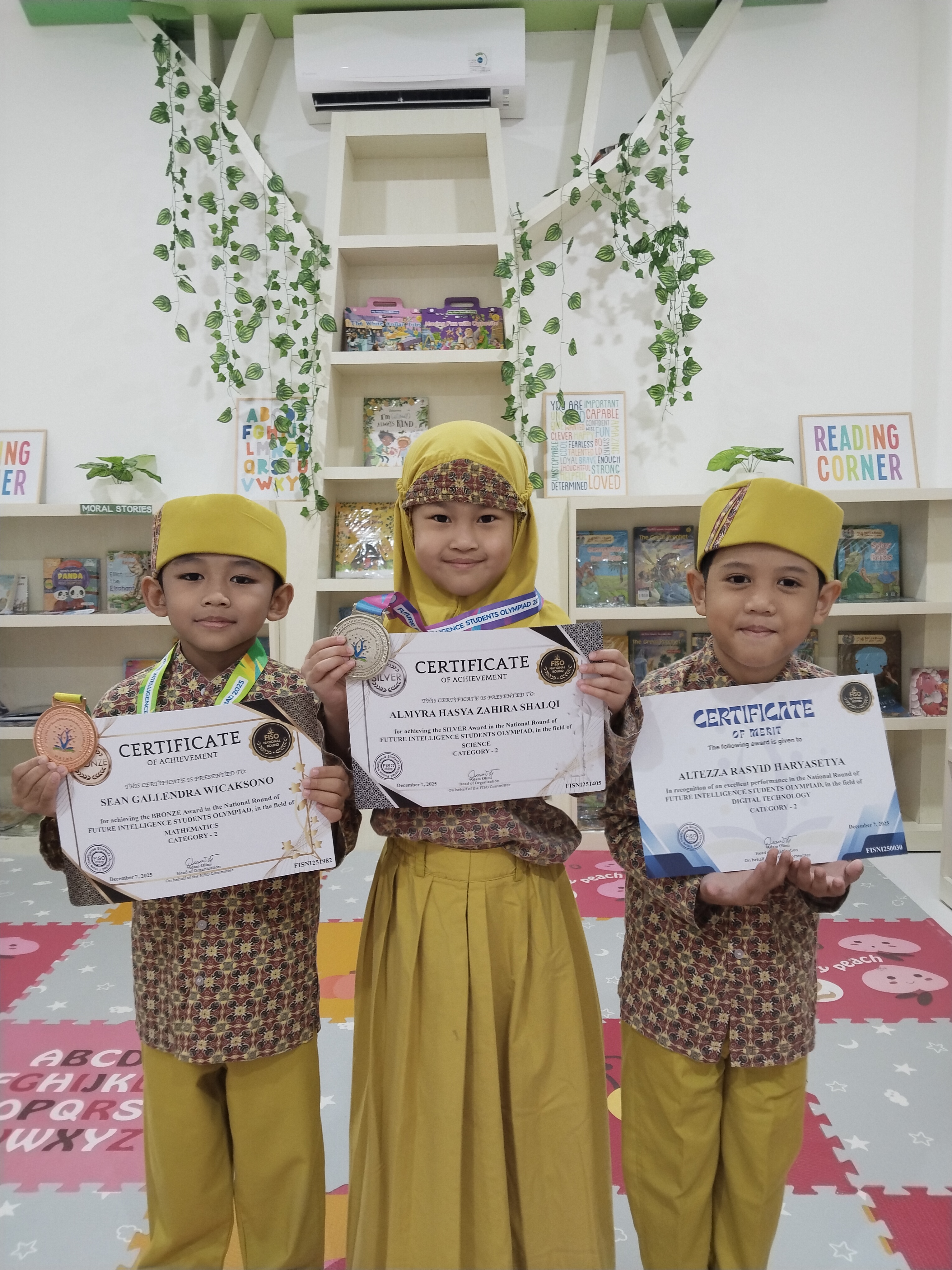 Three students holding their FISO certificates and medals in the reading corner
