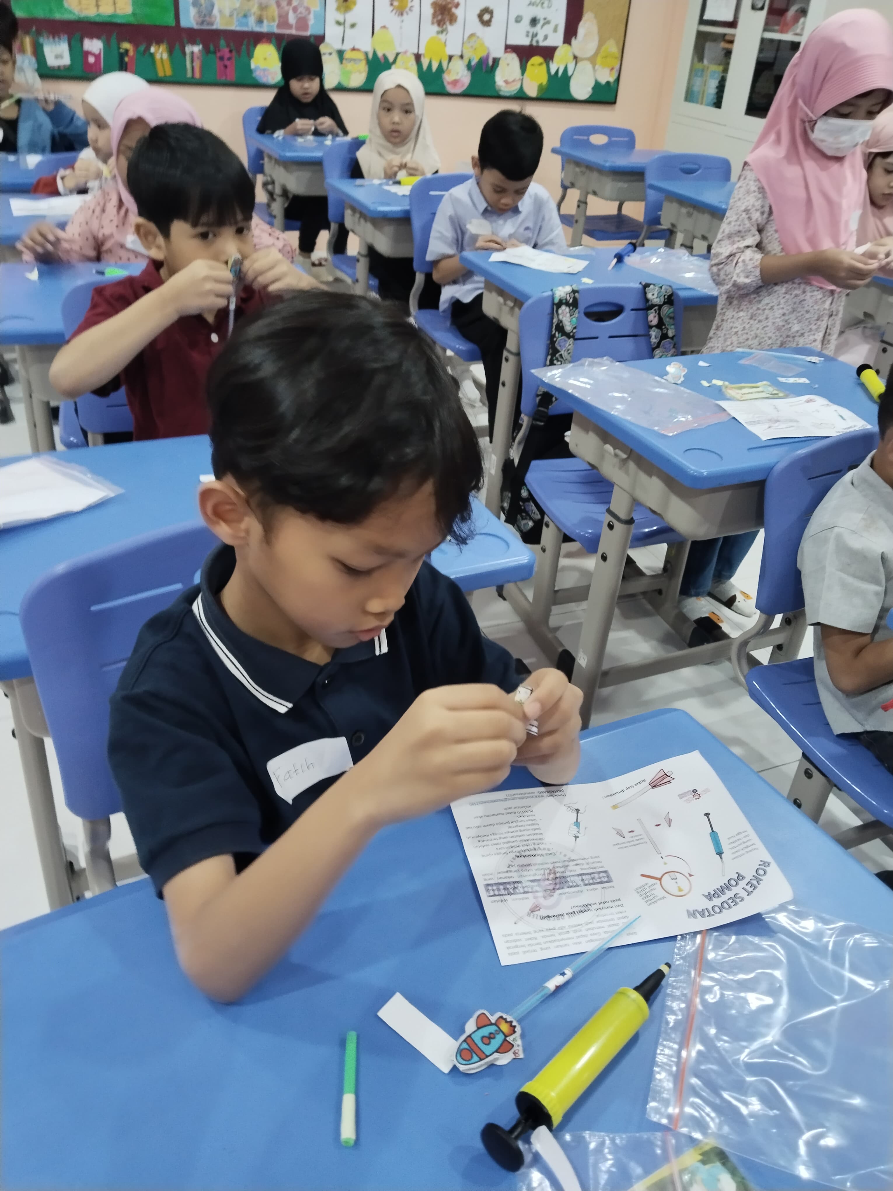 Students building straw-and-pump rockets at their desks during a science workshop